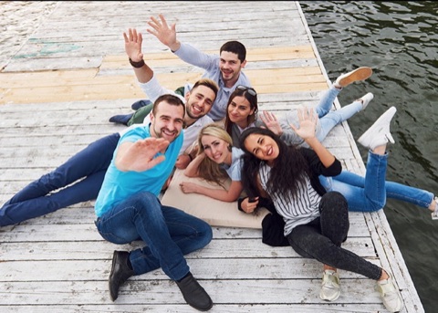 Six friends waving from a wooden dock, photographed from above